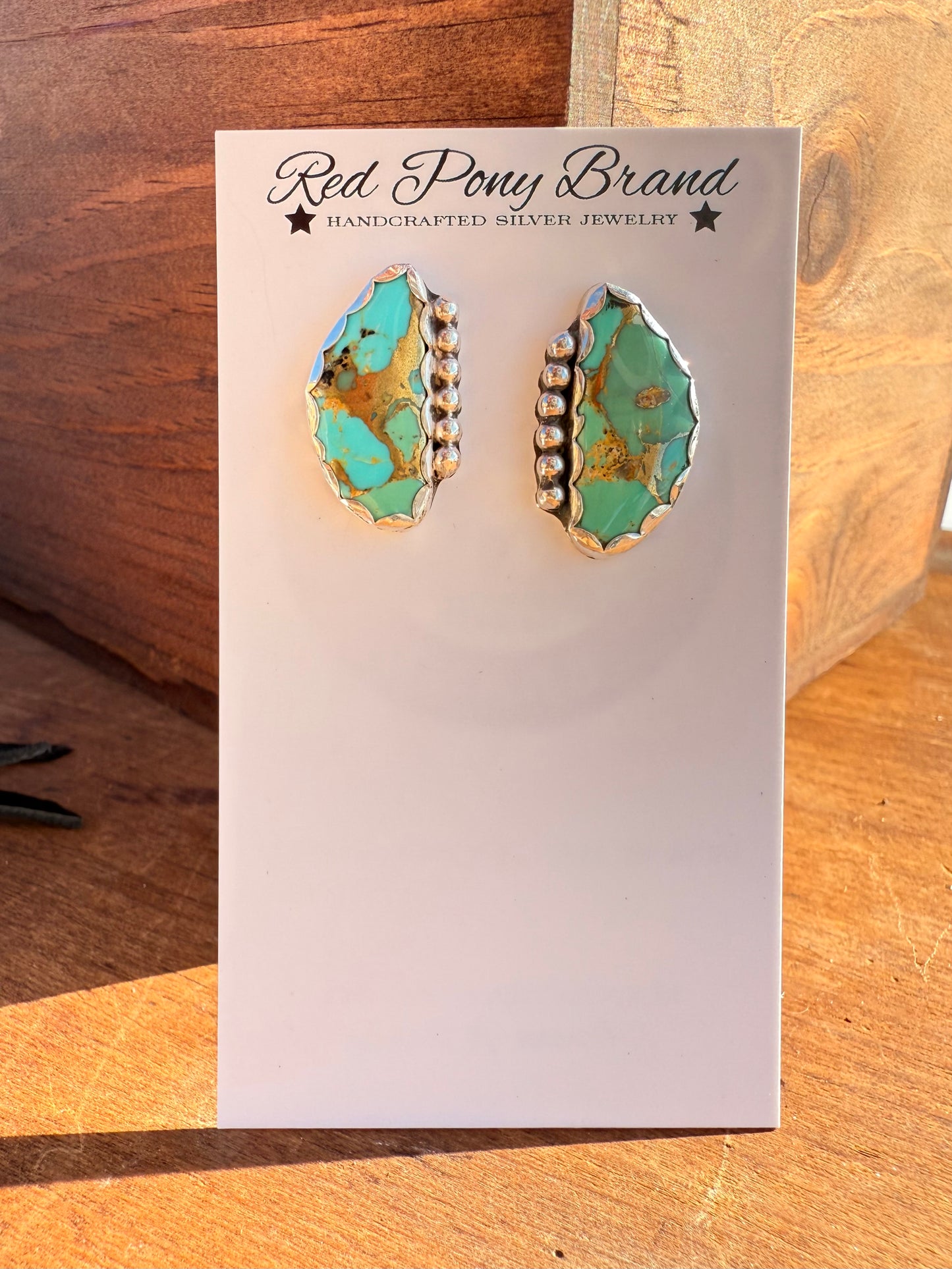 Red Pony Brand mohave turquoise bonded with bronze stones in silver earrings on a card with wood background