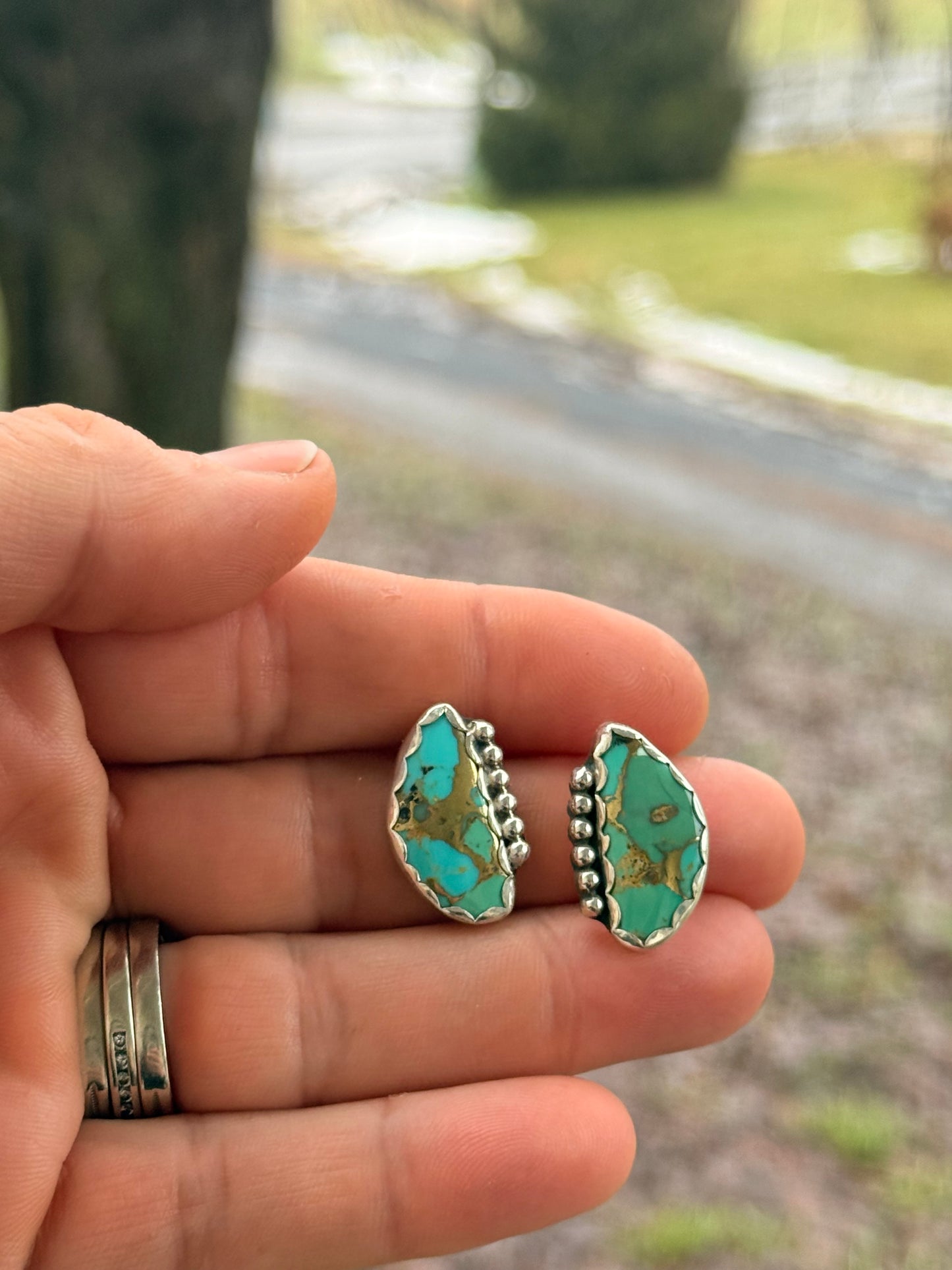 Red Pony Brand mohave and bronze earrings with a blurry outside background of lawn and trees