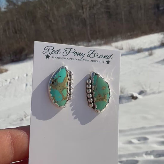 Red Pony Brand mohave turquoise earrings on a card held in a hand with a winter background