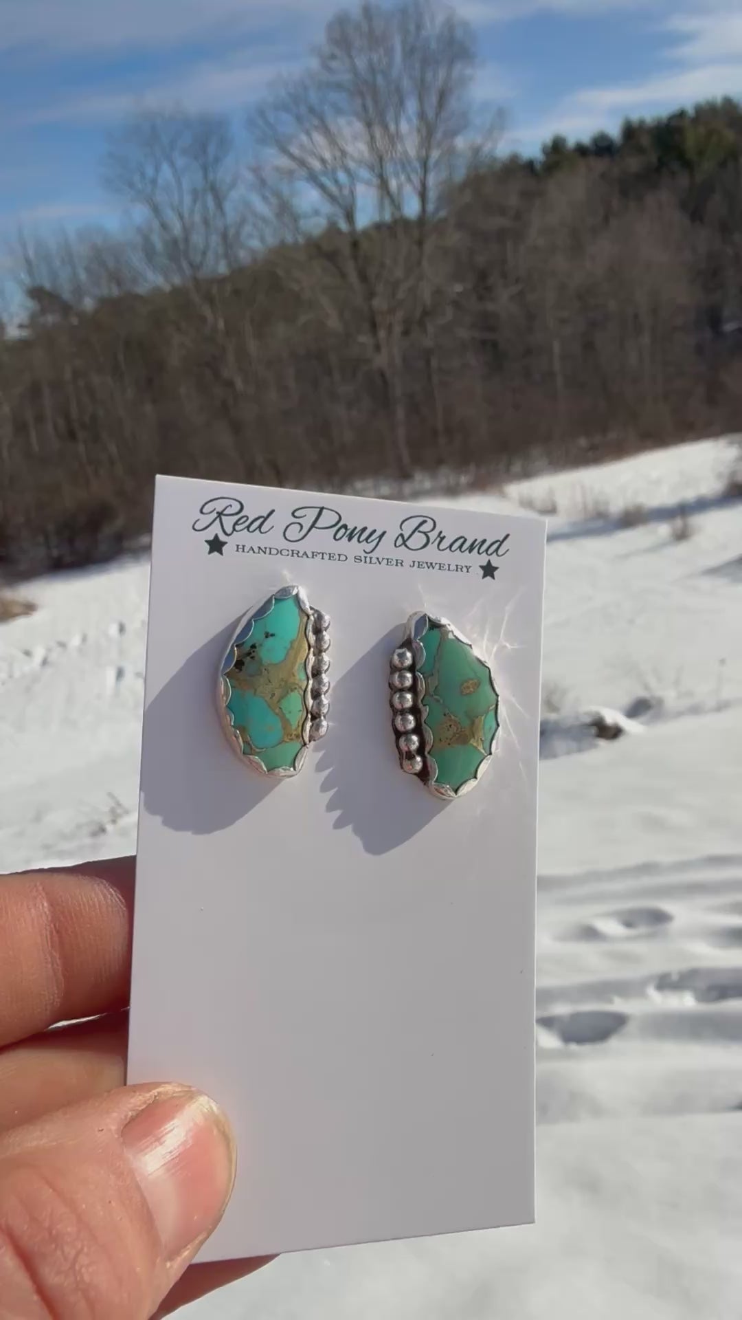 Red Pony Brand mohave turquoise earrings on a card held in a hand with a winter background